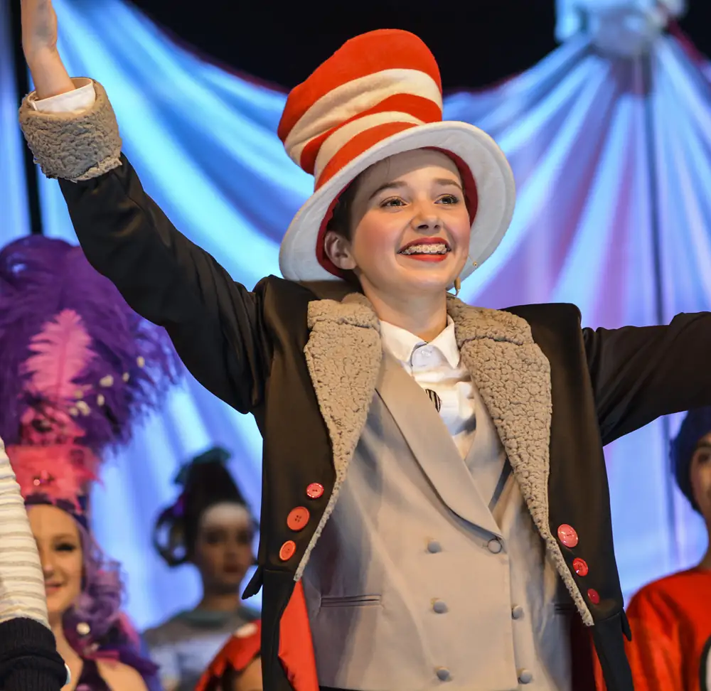 A young performer in a striped hat with arms wide, beaming