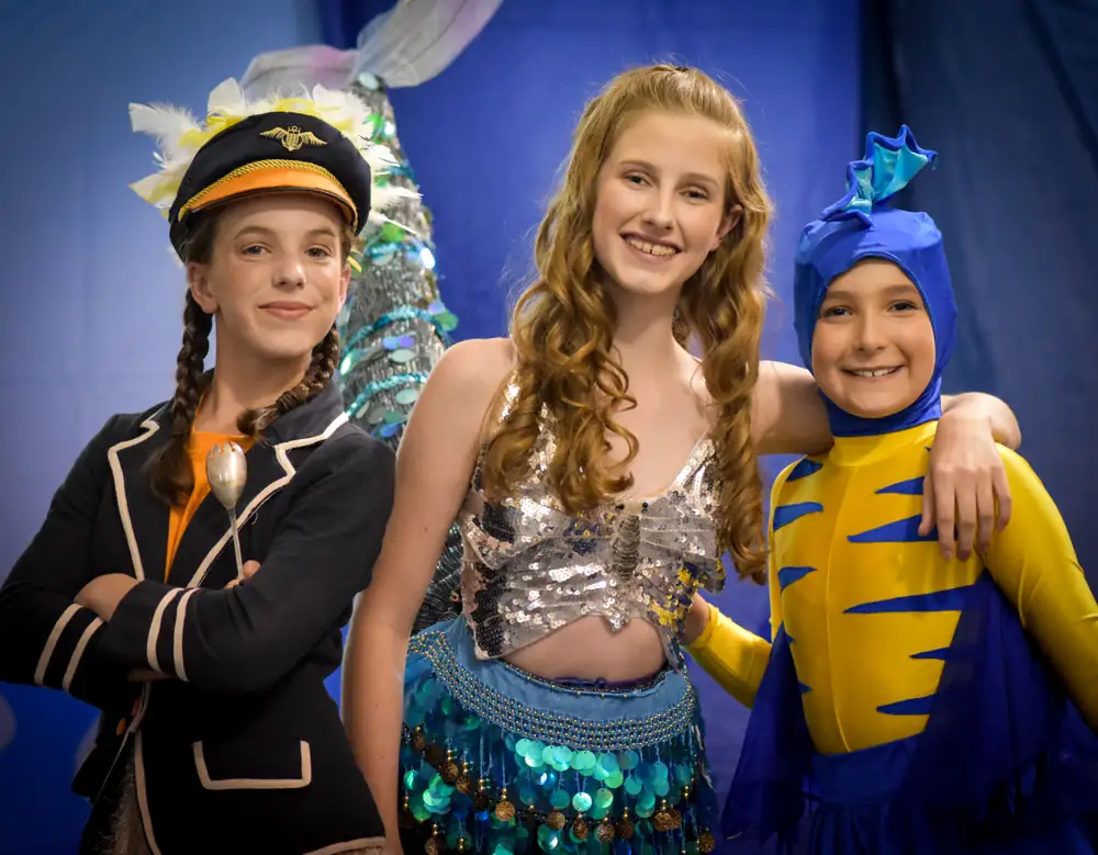 Three young performers in Little Mermaid costumes, smiling