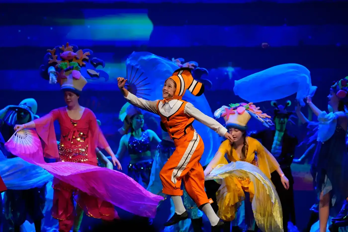 A performer in a clownfish costume dancing among colourful sea-creature costumes in Finding Nemo