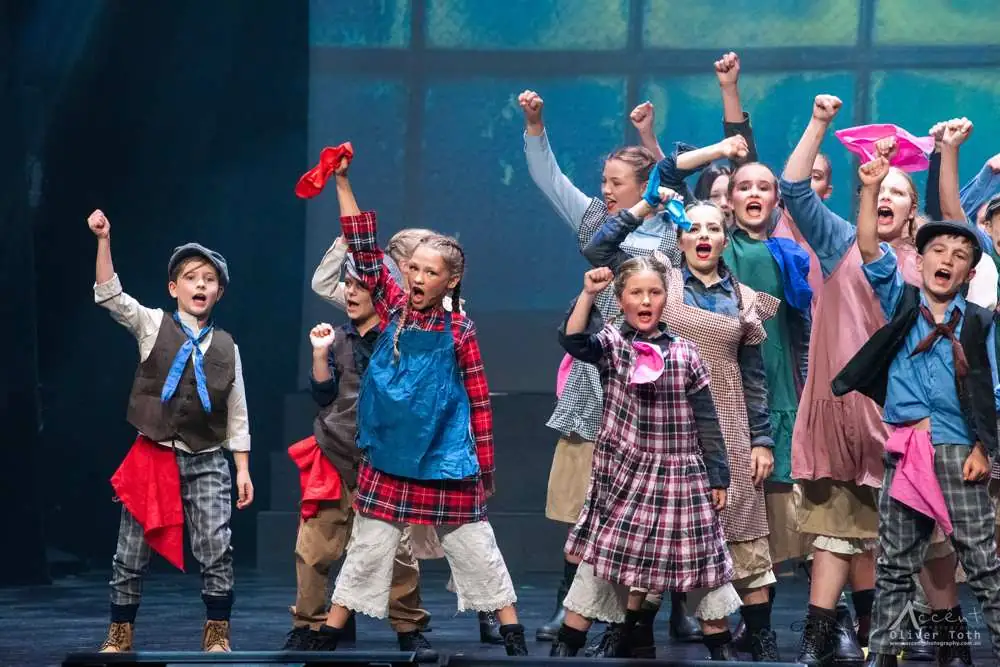 Young performers in patched costumes, fists in the air