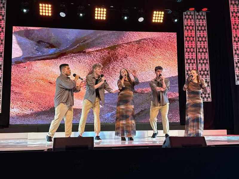 A vocal group in earthy tones against a red-rock screen
