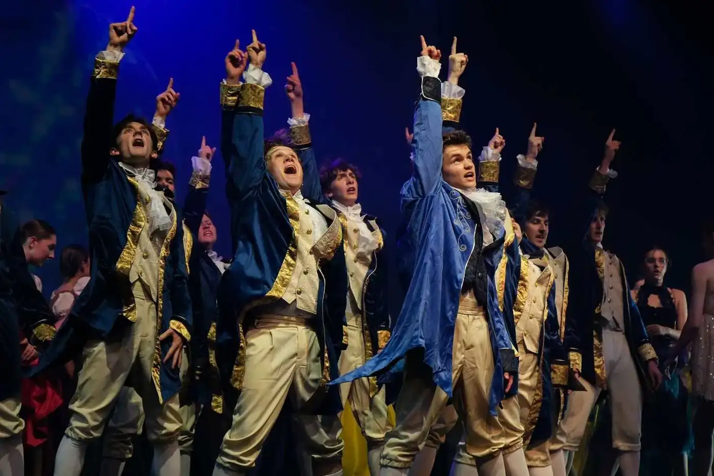 Pelican performers in blue and gold costumes under blue stage lights