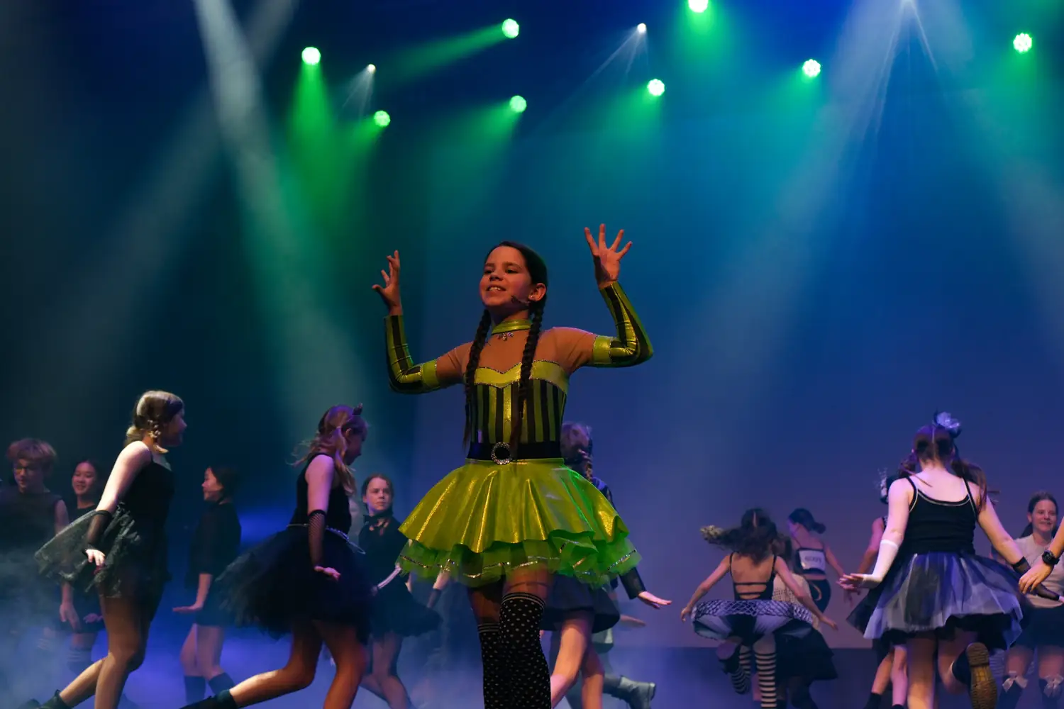 A young performer in a lime-green costume under green and blue stage lights