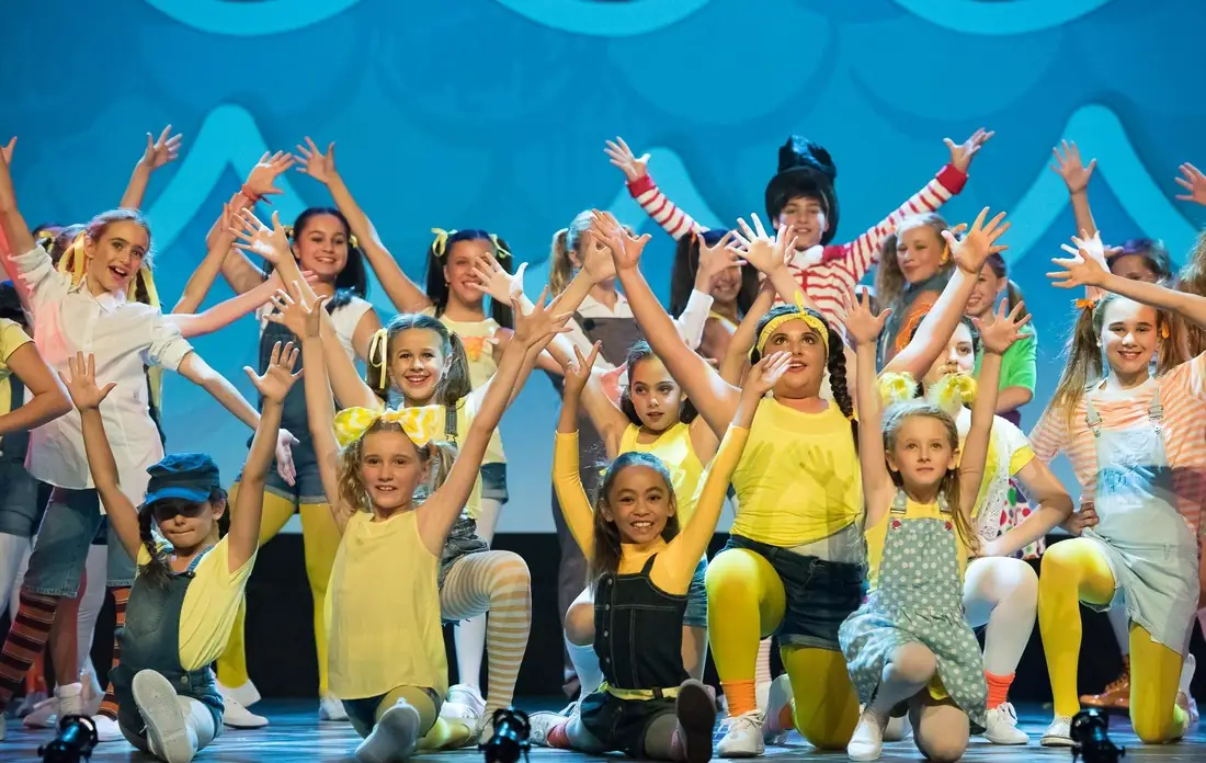 Young performers in yellow with arms stretched wide